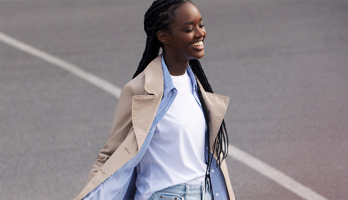 Une femme en trench-coat qui rit lors d'une promenade.