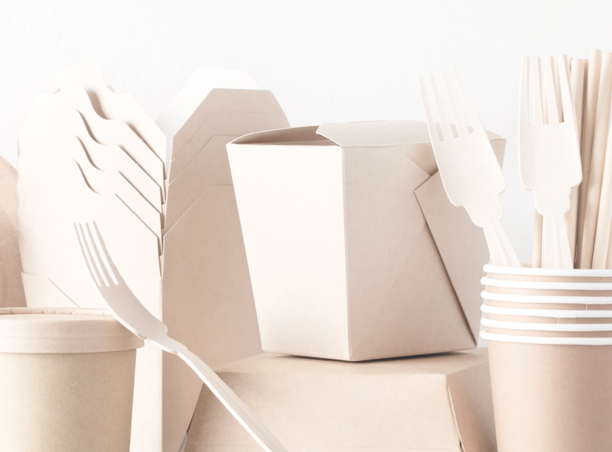 A glass of soda, and reusable utensils, cups and plates resting on a table.