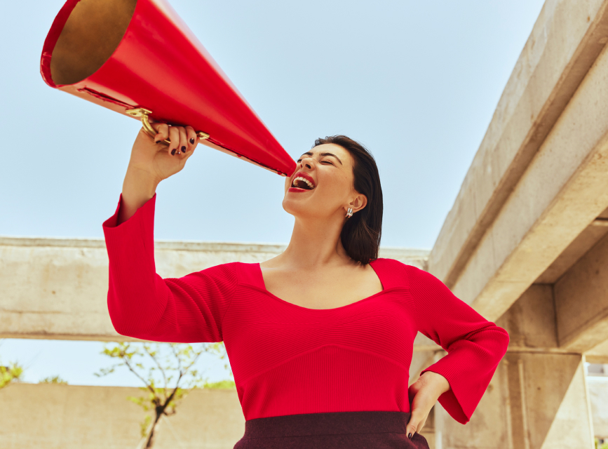 Une femme vêtue d'un haut rouge criant dans un haut-parleur rouge.