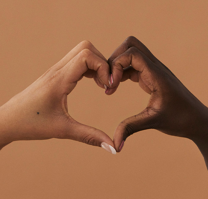 Two hands of contrasting skin tones form a heart.