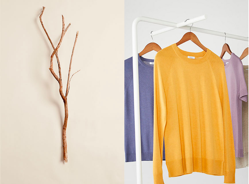 A long thin tree branch. Four sweaters hanging on a white rack.