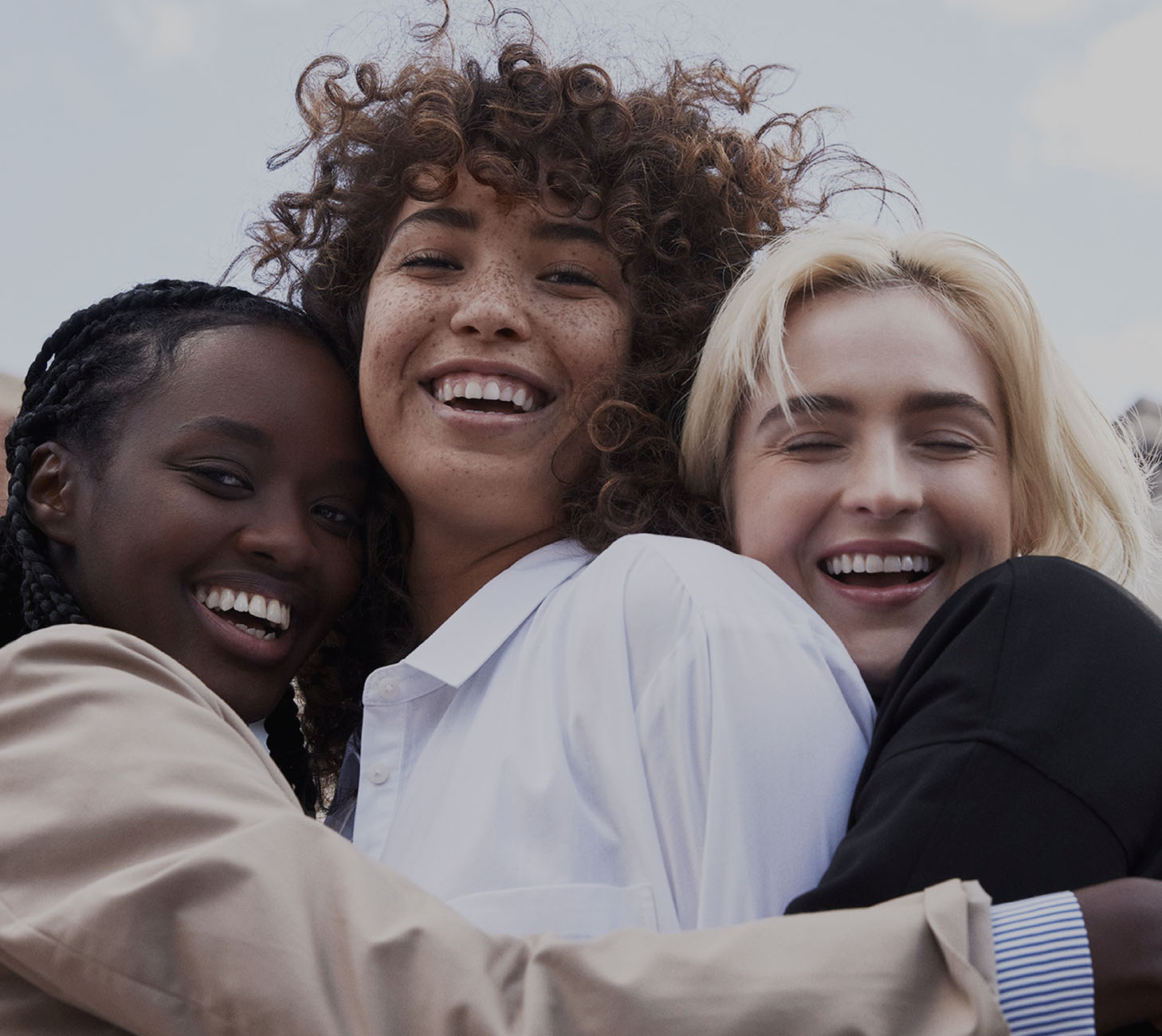 Three women hugging in front of a white sky.