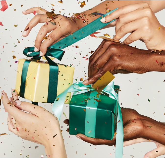 Five women's hands tying the ribbons on two presents.